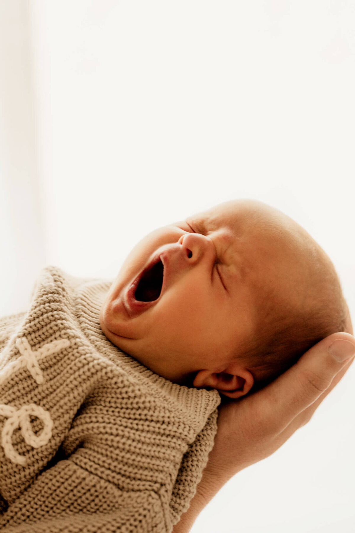 Newborn baby boy wearing a sage sweater yawns.