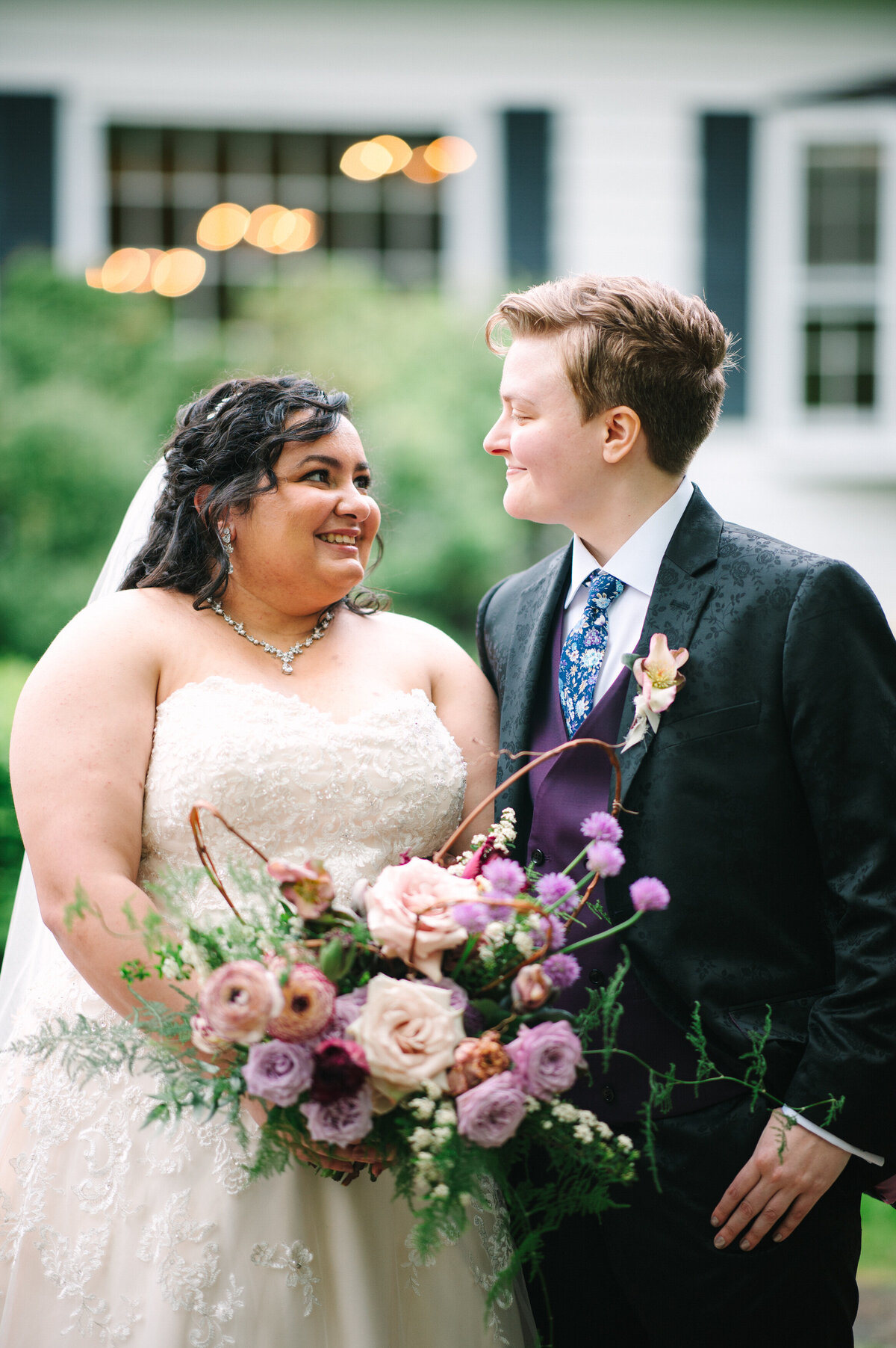 Two brides smiling at each other with purple bouquet
