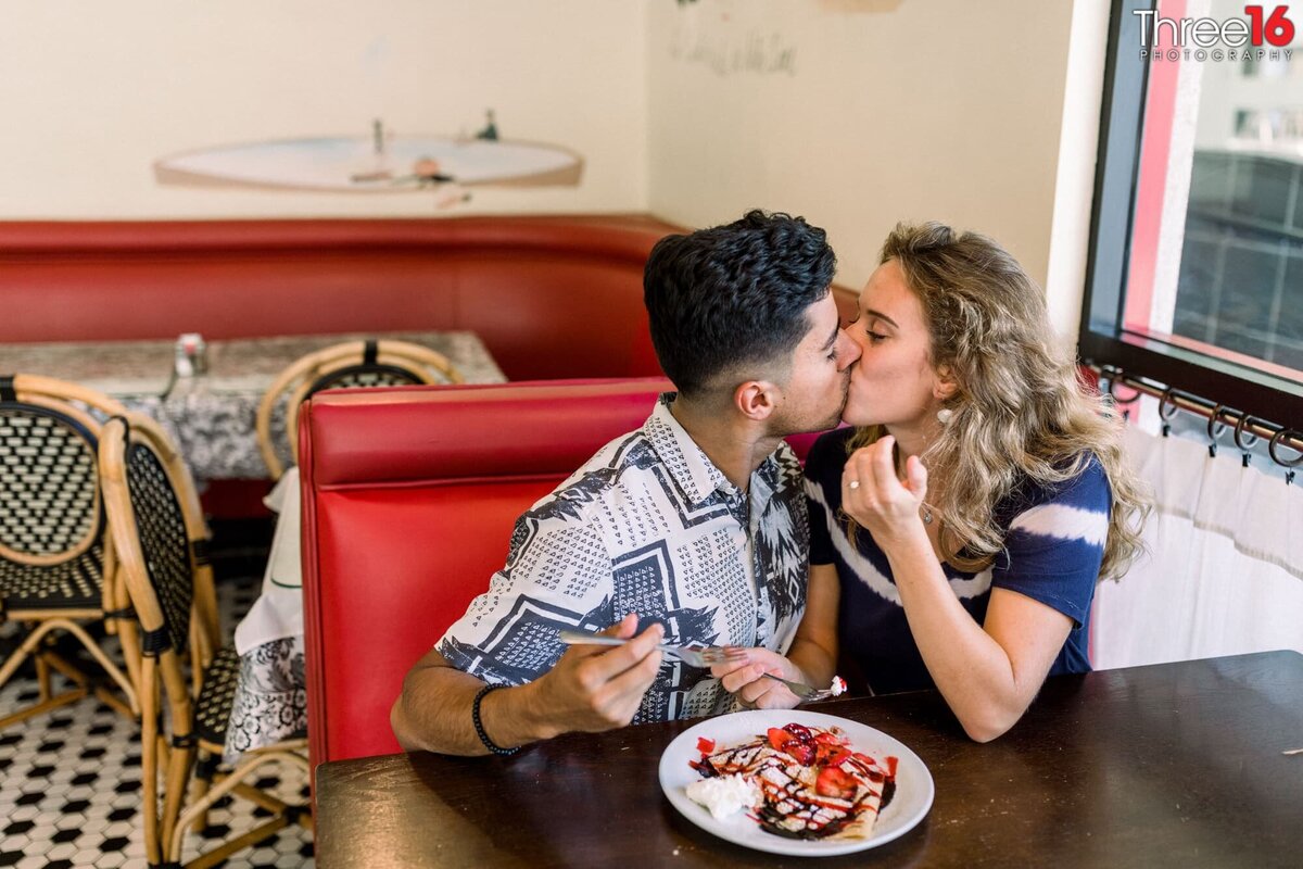Engaged couple sit in a booth before eating and share a kiss