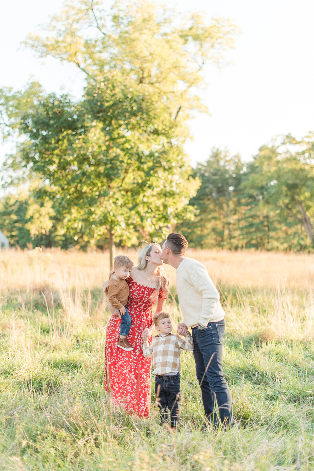 family of four kissing in a field at sunset