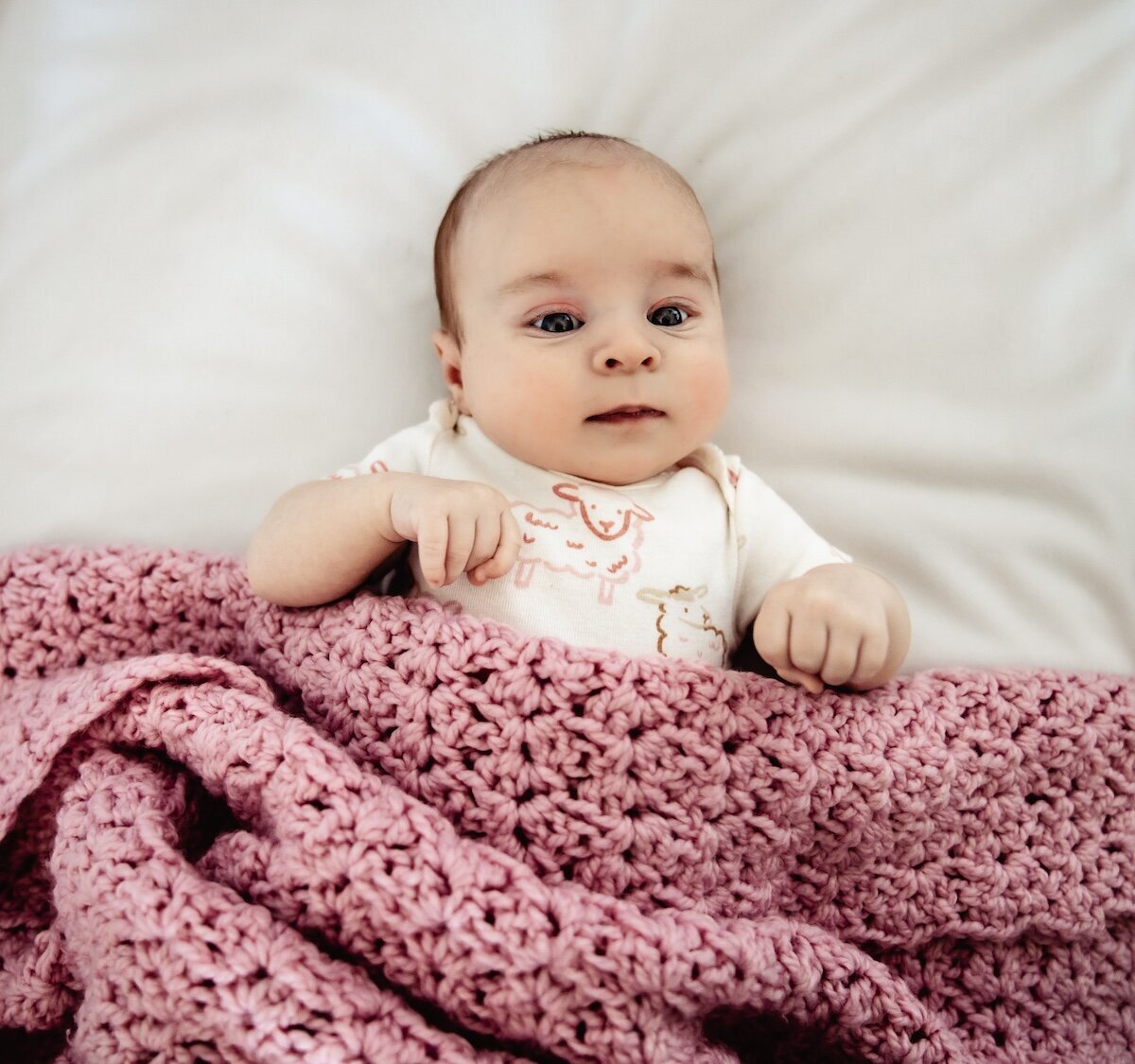 A newborn baby tucked in under a pink knitted blanket 