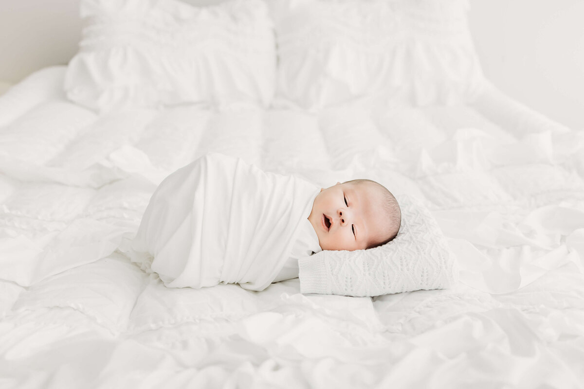 Newborn baby sleeping on bed in all white