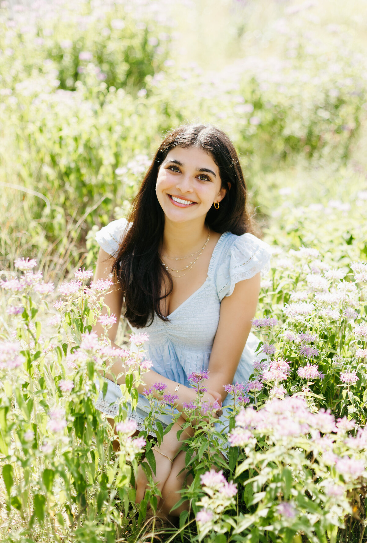 Senior girl in a blue top posing in a field of grassy flowers