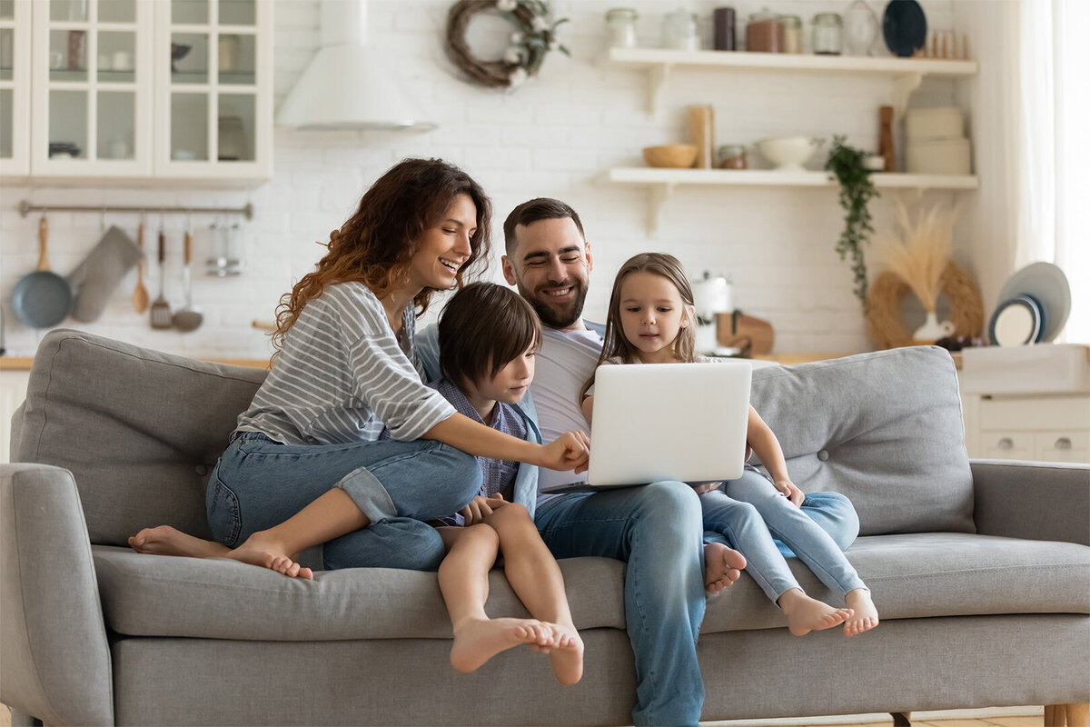 young family on couch smiling will working on computer
