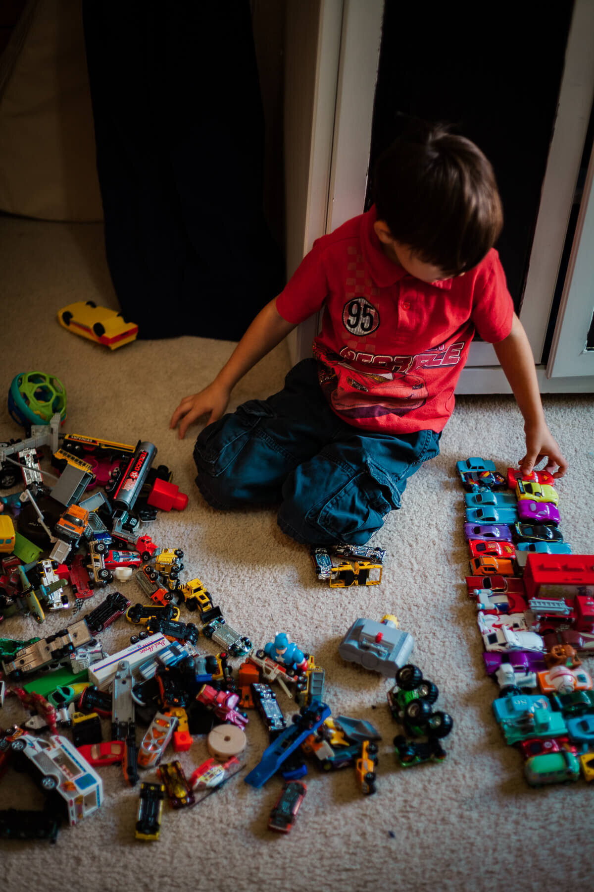 A boy plays with his toy racecar collection and organizes them into rows.