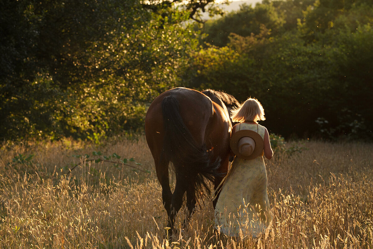 a woman and her horse are walking in the long grass in the field at sunset