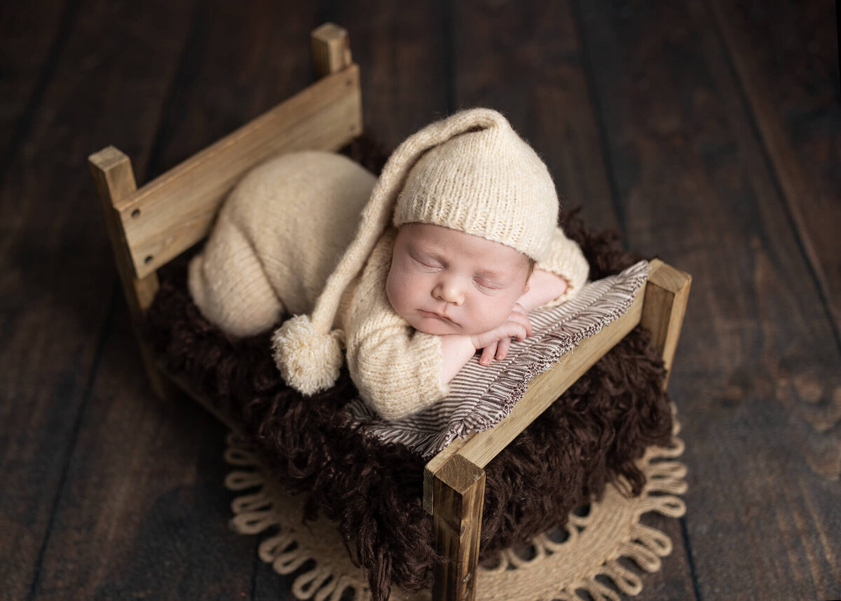 Newborn boy safely posed on a wooden bed at Jennifer Brandes Photography.