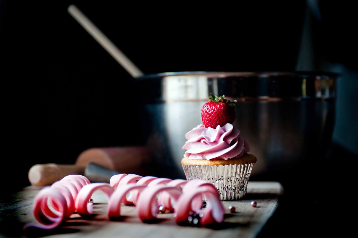 A strawberry cupcake with baking materials and mixing bowl and rolling pin make a perfect setting for photographing cupcakes