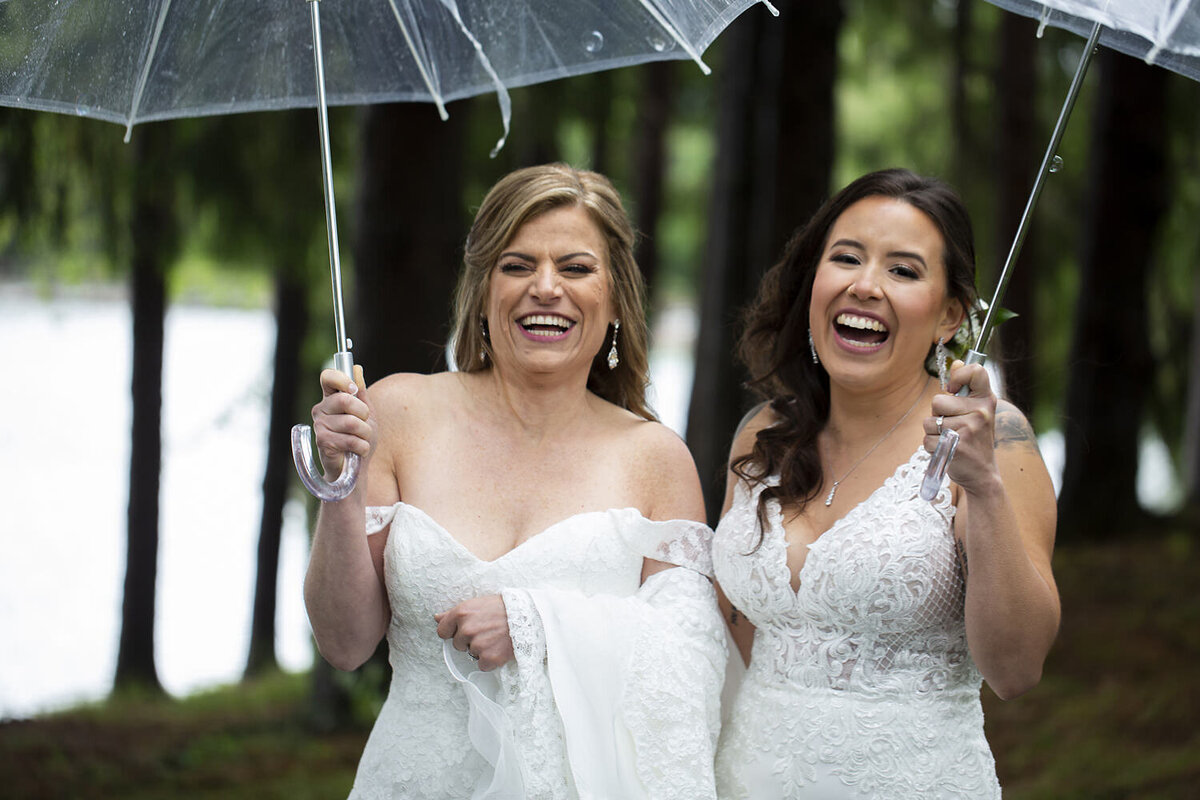 A newlywed couple laughing as they both hold clear umbrellas 