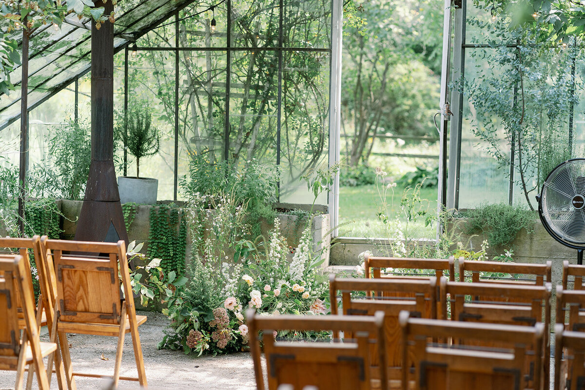 Glasshouse Community greenhouse ceremony setup with wooden chairs, lush greenery, and natural light for a romantic Michigan summer wedding.