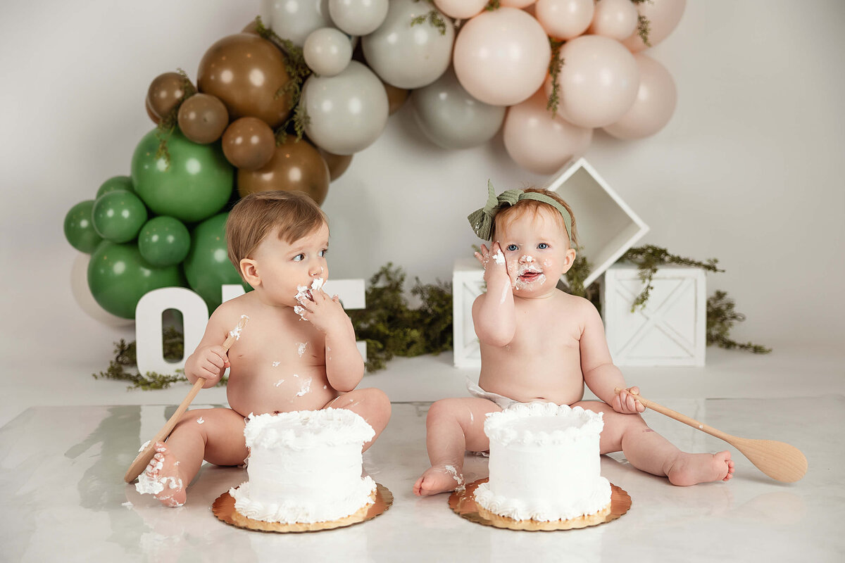 Twin one-year-olds get their first taste of frosting from their smash cakes during their one year portrait session.