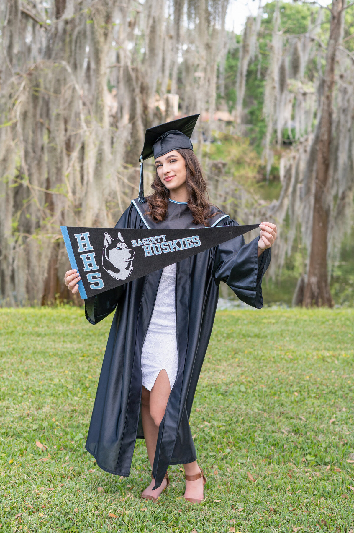 High school senior girl in cap and gown holds a Hagerty Huskies pennant.