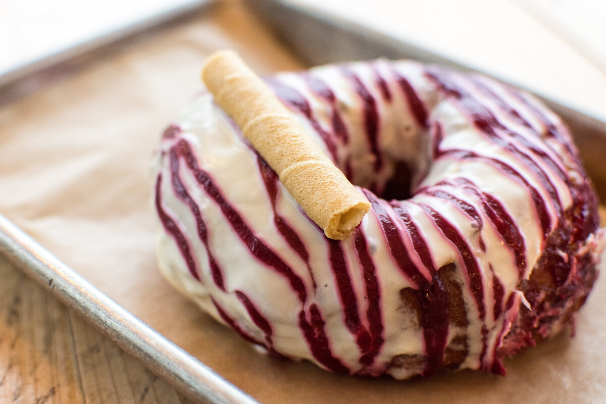 Closeup image of a dark red and white frosted donut with a vanilla pirouette rolled wafer cookie on top