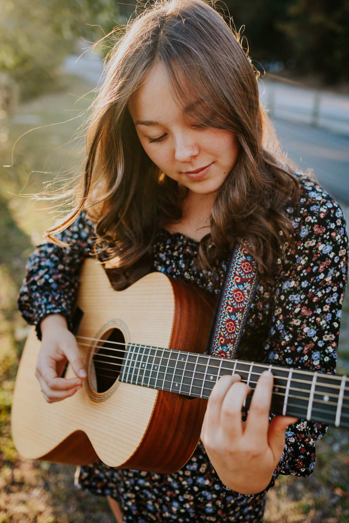 Young woman looks down at guitar as wind tousles her hair.