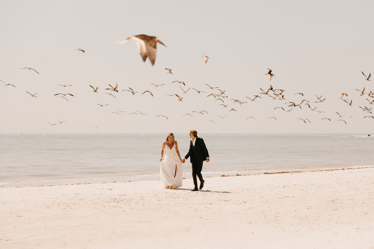 couple running through birds on the beach in florida