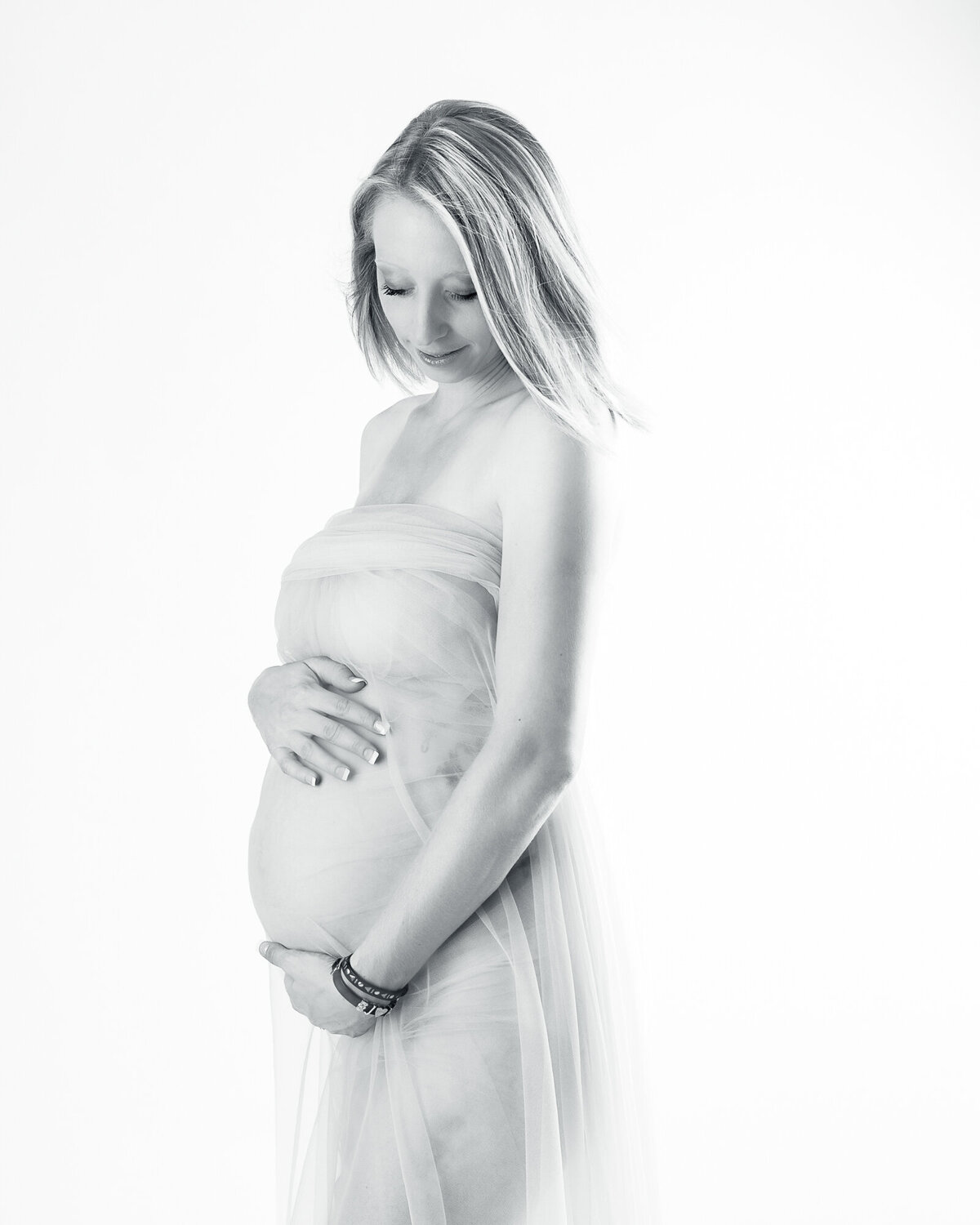 Black and white photo of a pregnant woman wearing a  shear wrap with her hands on her belly