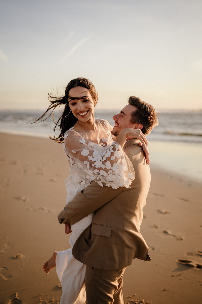 Un couple de jeunes mariés s’enlace et rit sur la plage au coucher du soleil, le soir de leur mariage près du Domaine de Petiosse, capturé en duo photo et vidéo.