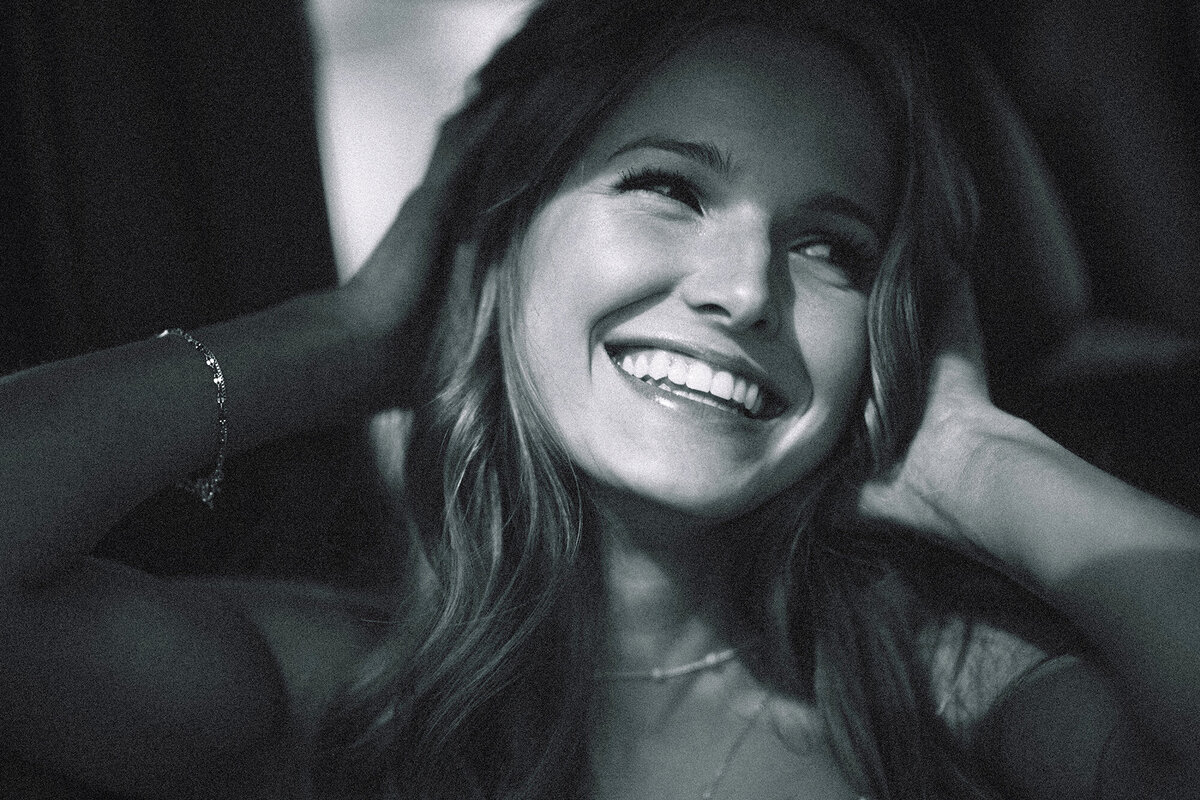 A black and white closeup image of a high school senior smiling with hands in hair