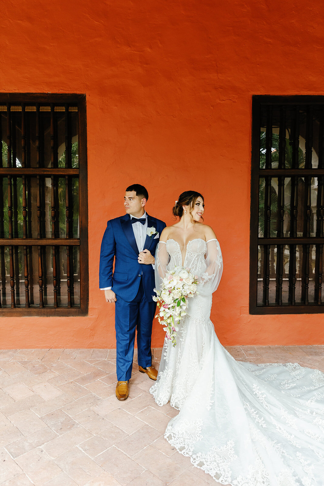 Victoria and Daniel stand hand-in-hand against a pastel wall in Cartagena, a stunning backdrop for their destination wedding.