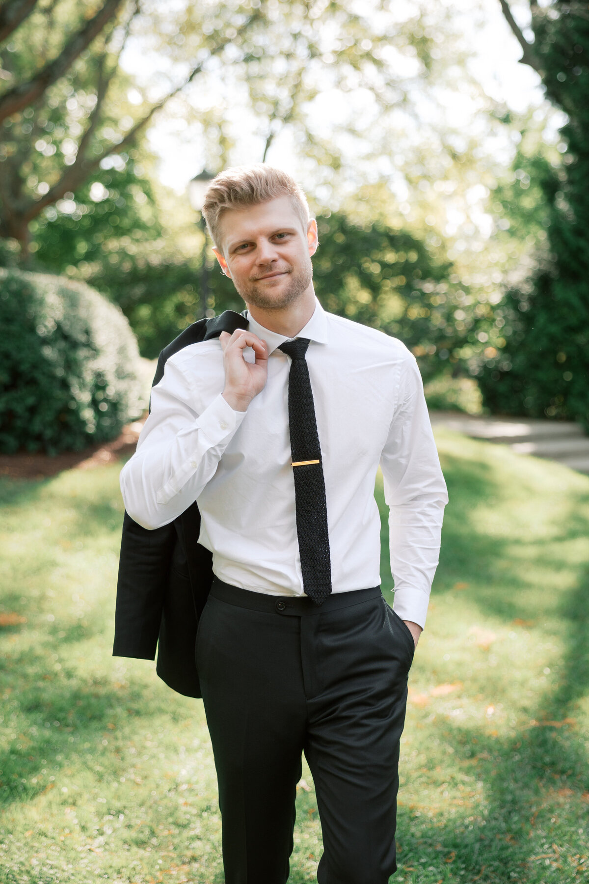 Groom walking with jacket over shoulder during Dayton, Ohio wedding, photographed by a Philadelphia-based artist.