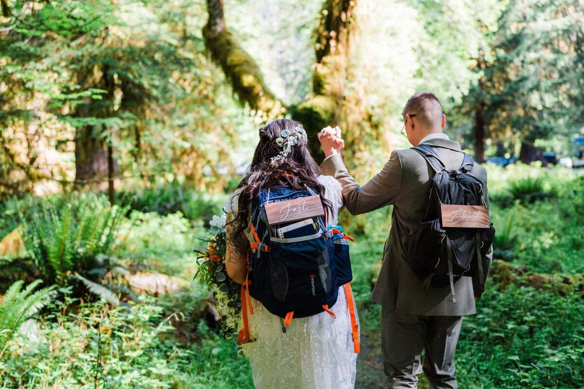 Couple hiking through the forests of Washington wearing backpacks that say "Just eloped."