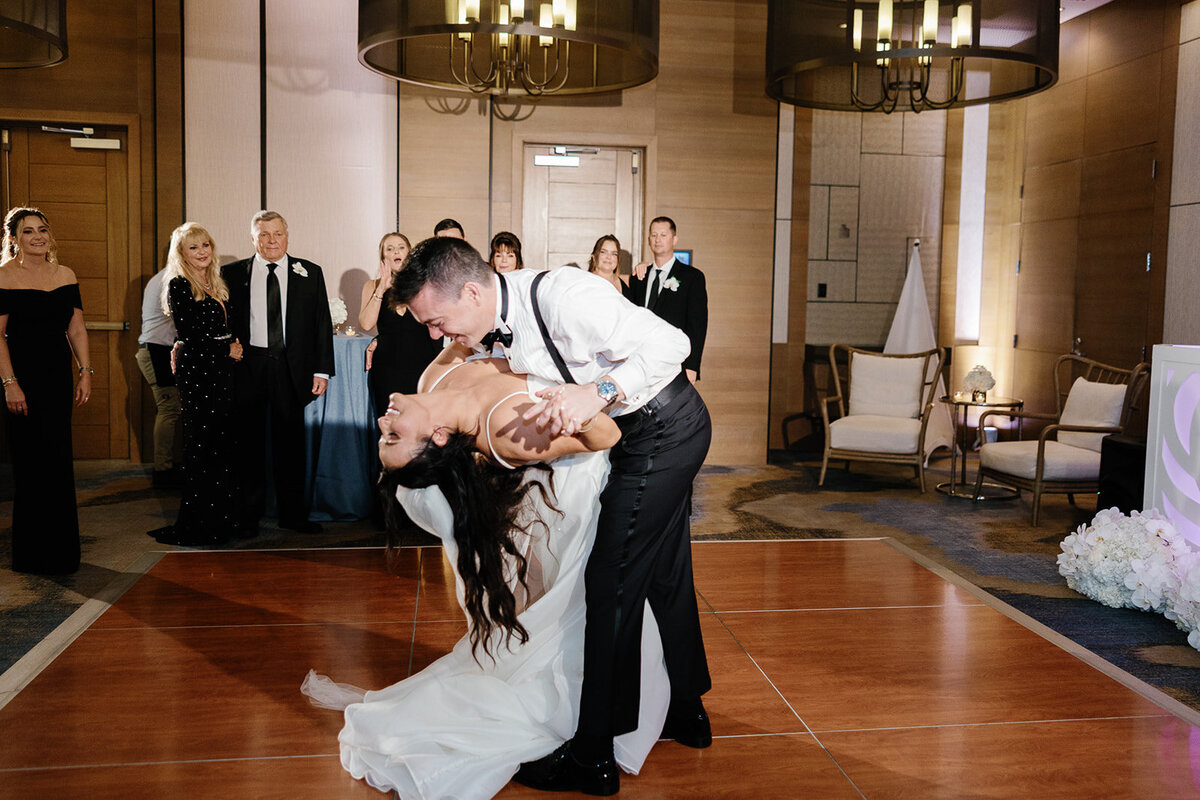 The groom dips the bride during their first dance as guests look on, adding drama to their Miami wedding celebration, captured by Claudia Amalia Photography.