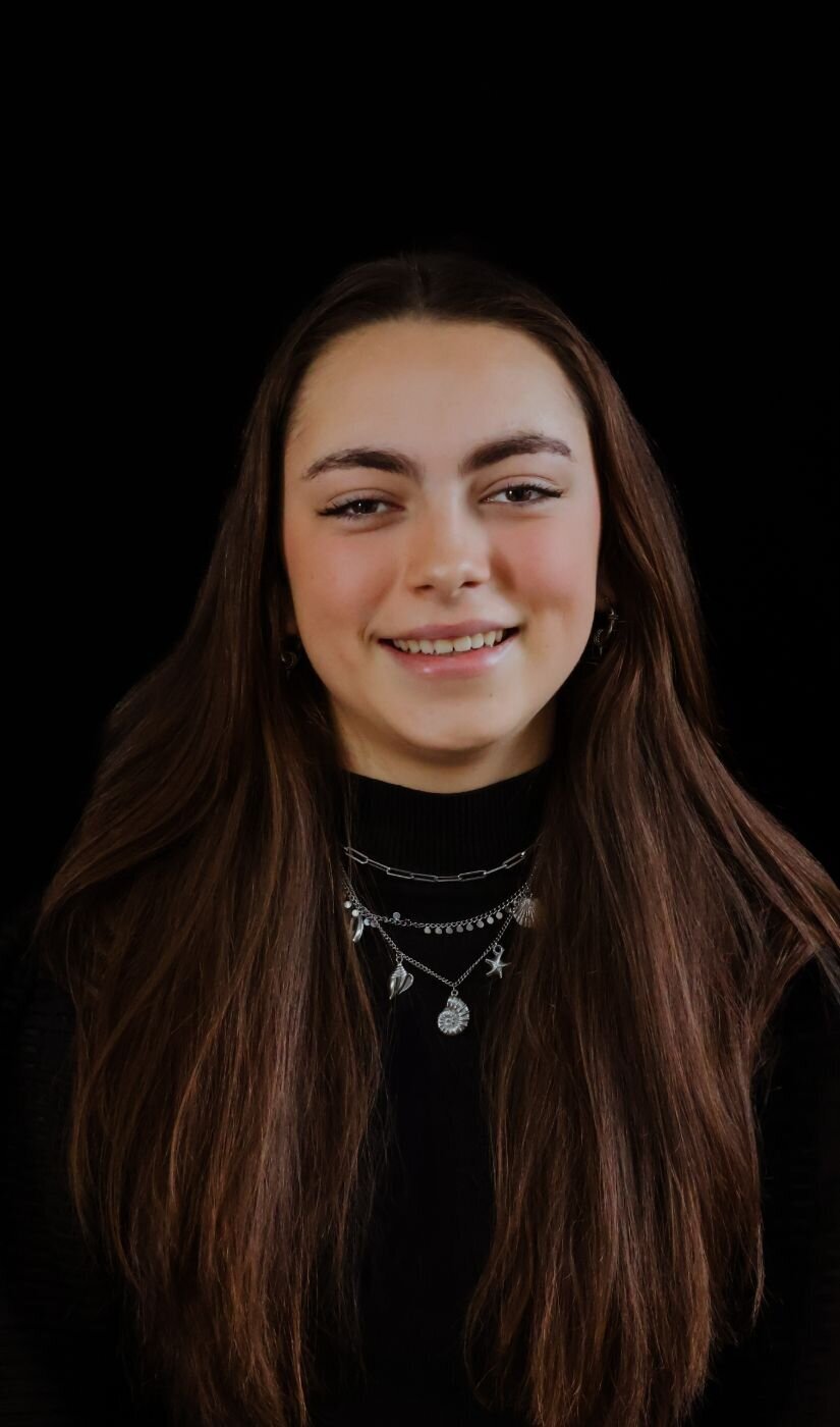 Een portretfoto van een meisje met lang haar en een stralende glimlach, gefotografeerd tegen een donkere achtergrond