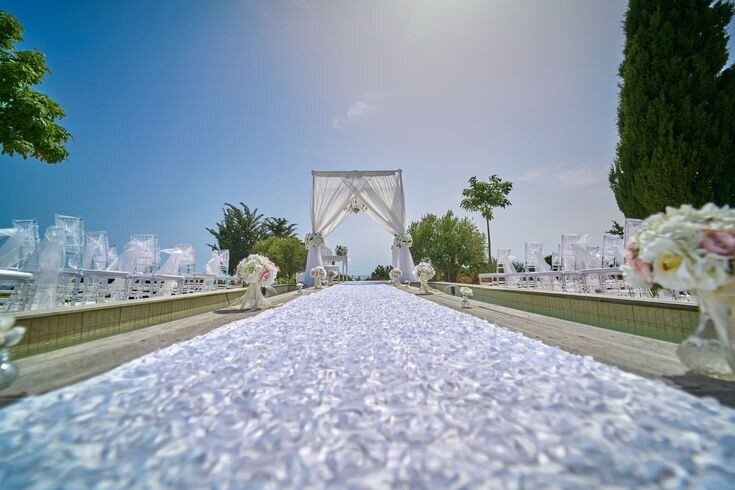 An aisle covered with white petals  leading towards a decorated arch under a clear blue sky