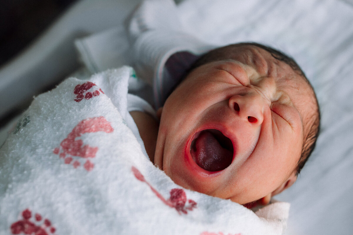 yawning newborn swaddled in hospital blanket and laying in bassinet