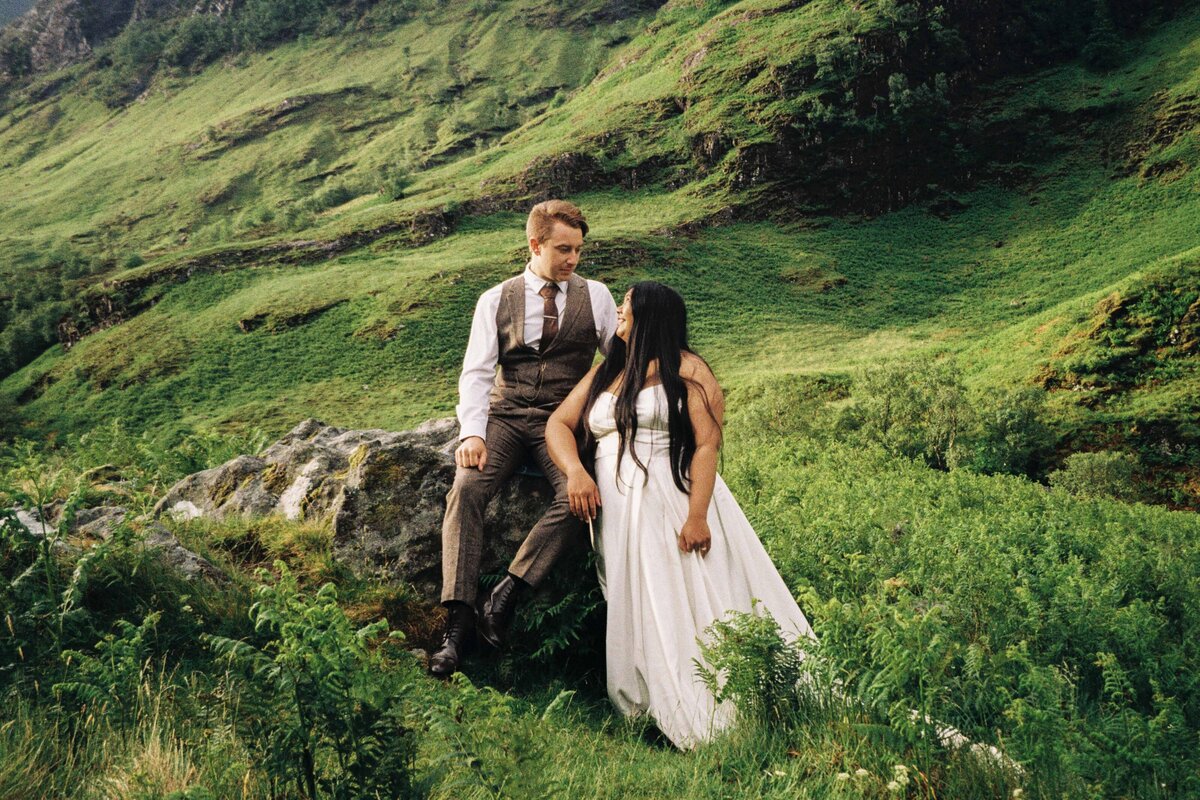 A bride and groom sit on a large rock in the Aberdeenshire countryside. The photo is taken on 35mm film.
