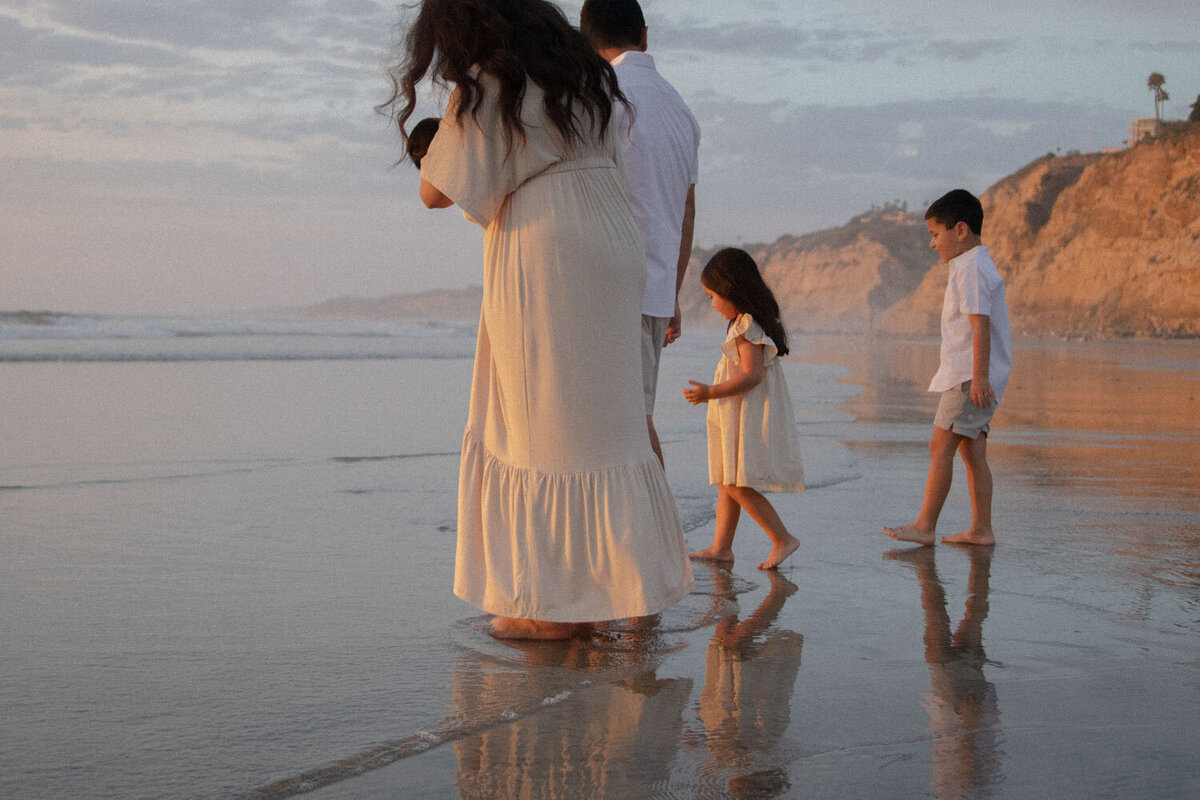 Family looking down at their footprints in the wet sand.