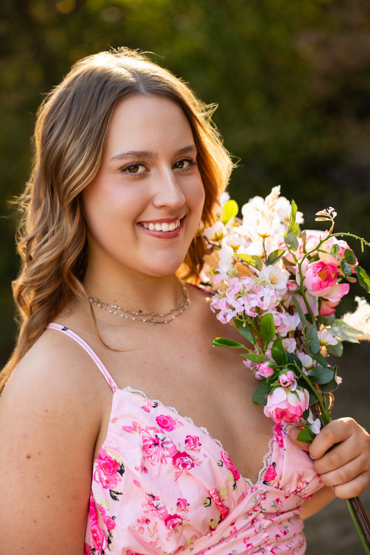 Senior girl in pink floral dress holding flowers smiling at camera in Lawrence KS
