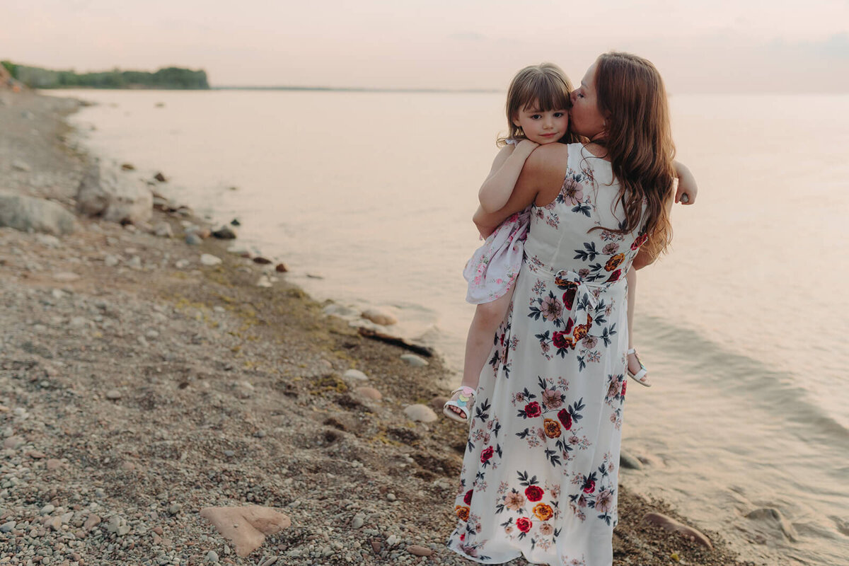 Woman carrying young girl at family with two kids on the beach at family photo shoot in Finger Lakes, NY