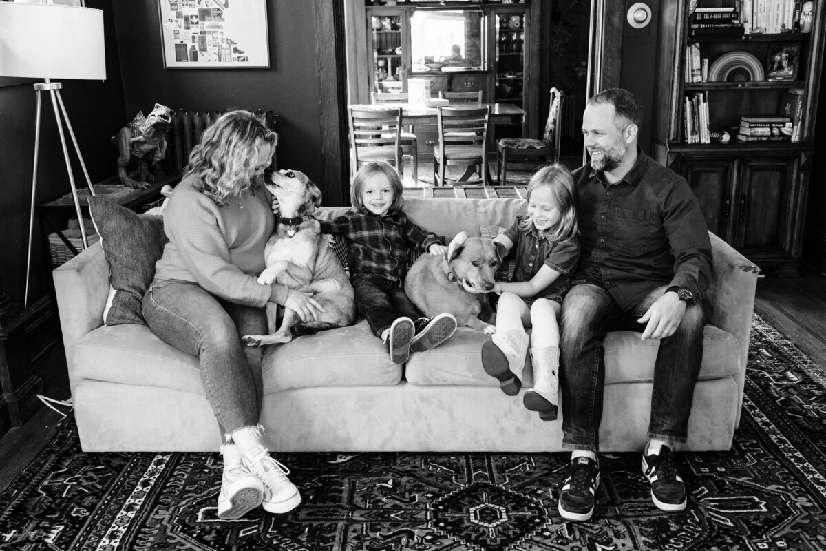 A family of four plus their dog sits on a couch.