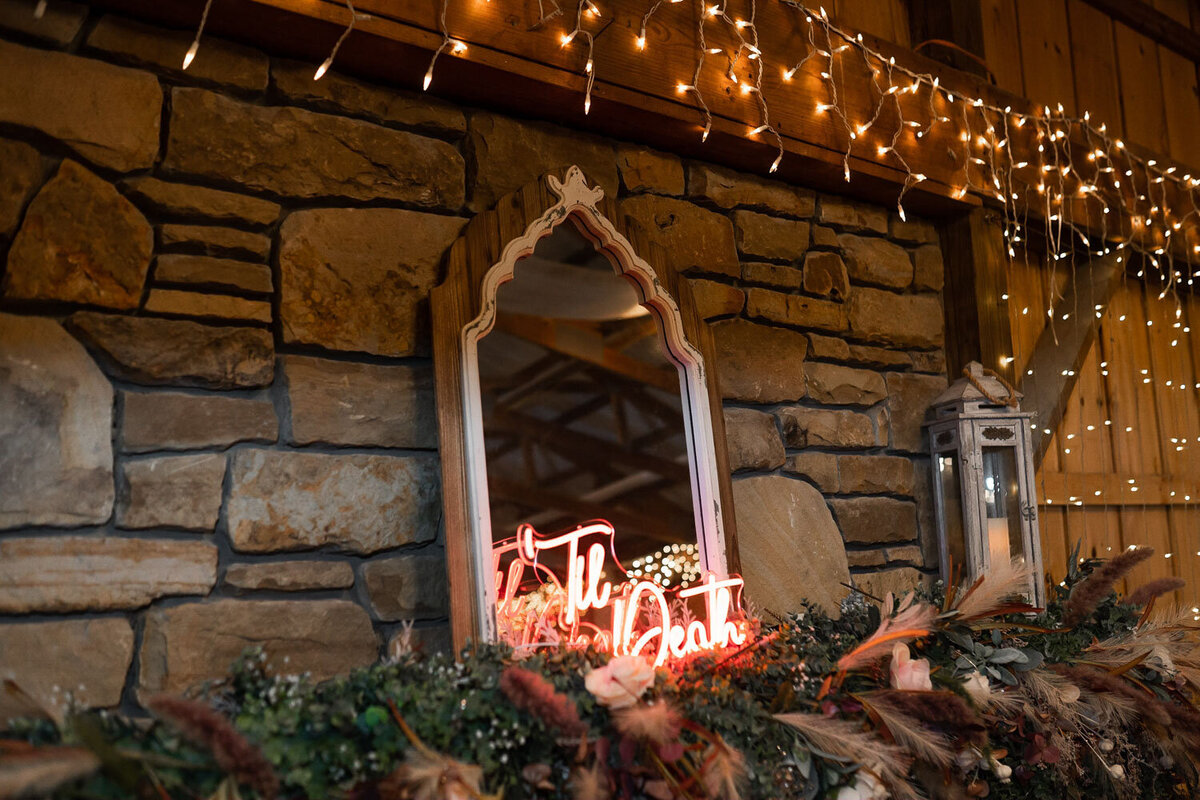 Neon "Til Death" sign on a stone fireplace with floral decor