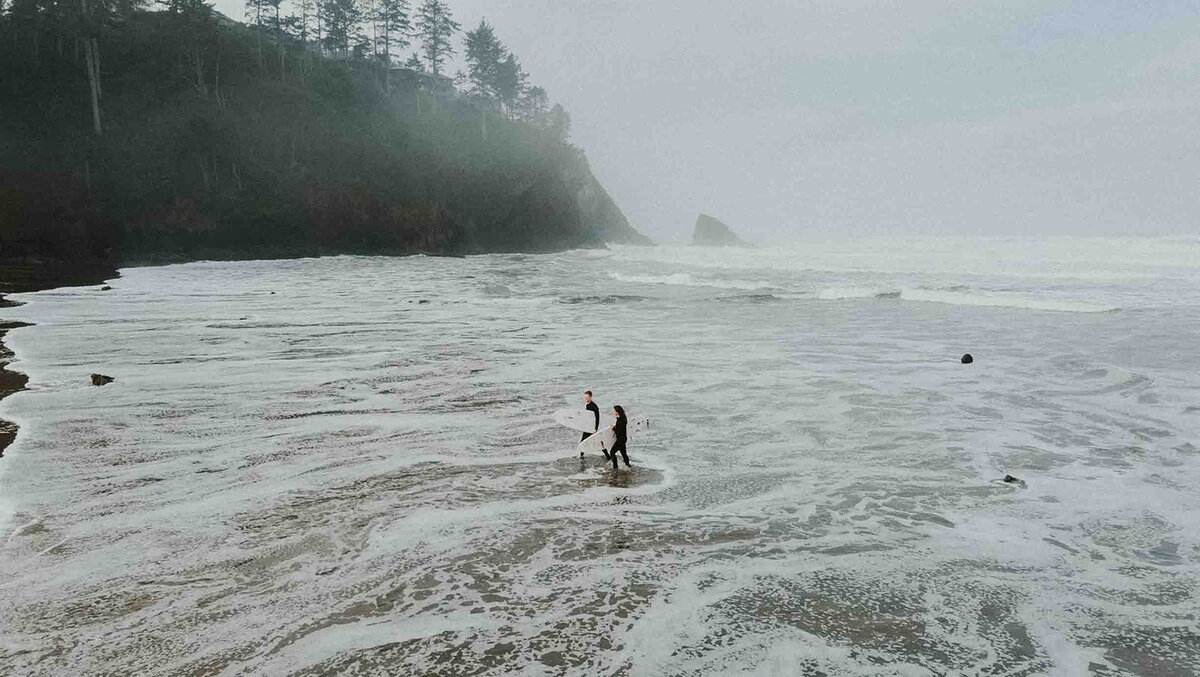 Two surfers walk in from the water at the PNW coast