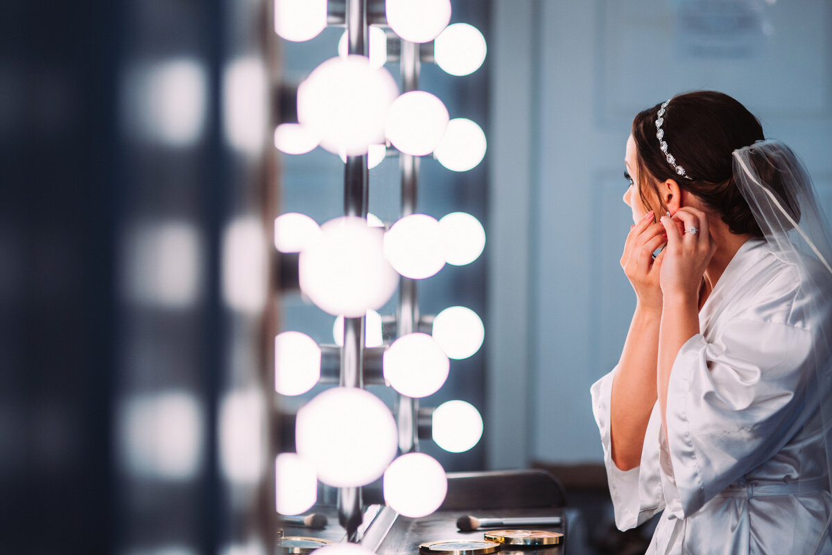 a bride with a veil and pearl head piece in a silk robe getting ready in the Willowbrook wedding venue preparation suites with lighted make-up mirrors