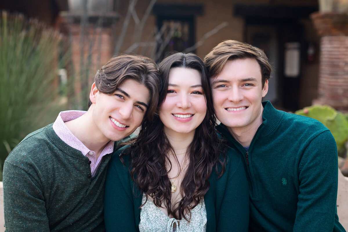 Two brothers smile with their heads against their sister in between the two of them, dressed in different shades of green.