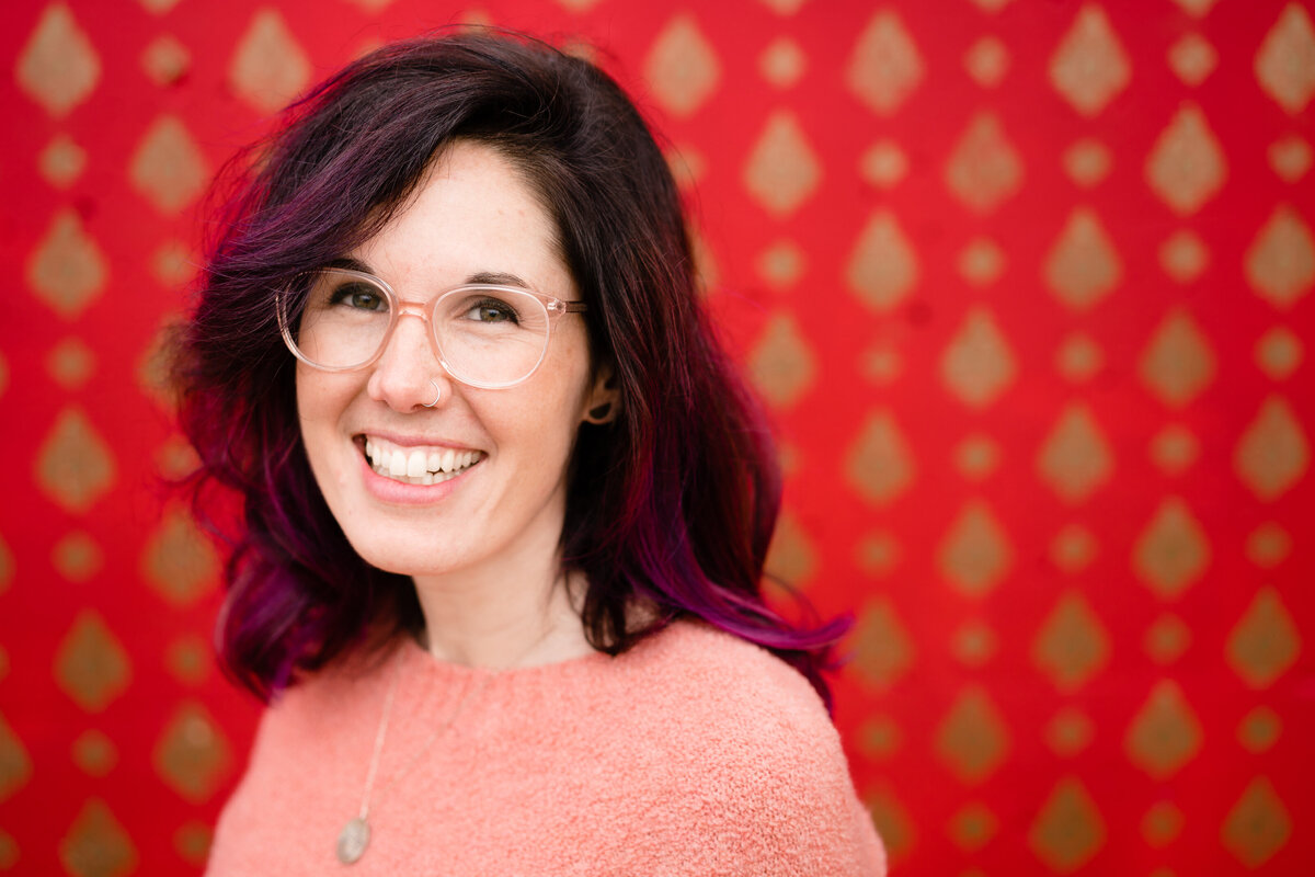 A person smiling while standing in front of a red wall with gold accents.