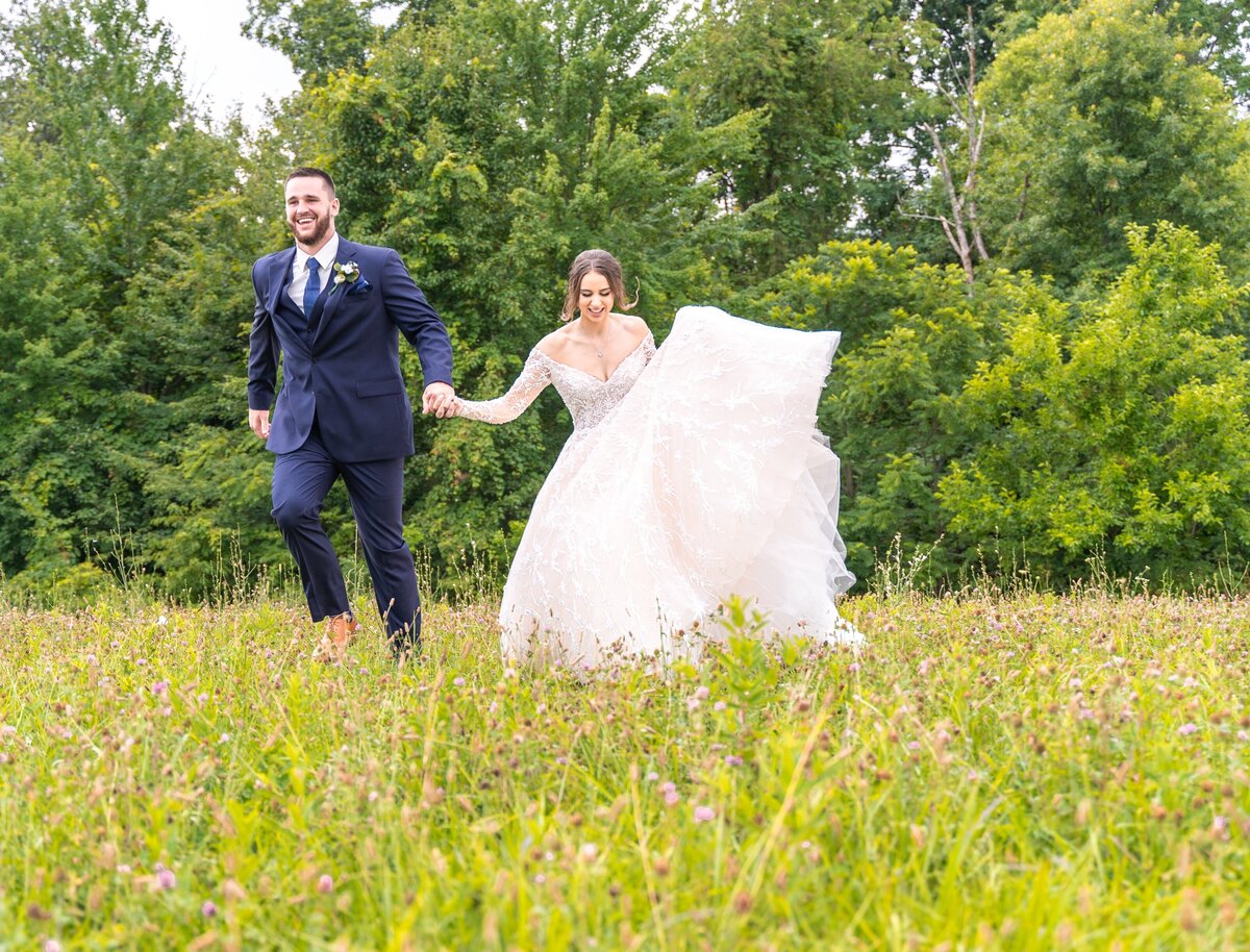 Bride and groom, Mahalie and Ryan Bee, run through a field on their wedding day at The Old Blue Rooster Events Center LLC in Lithopolis, Ohio.