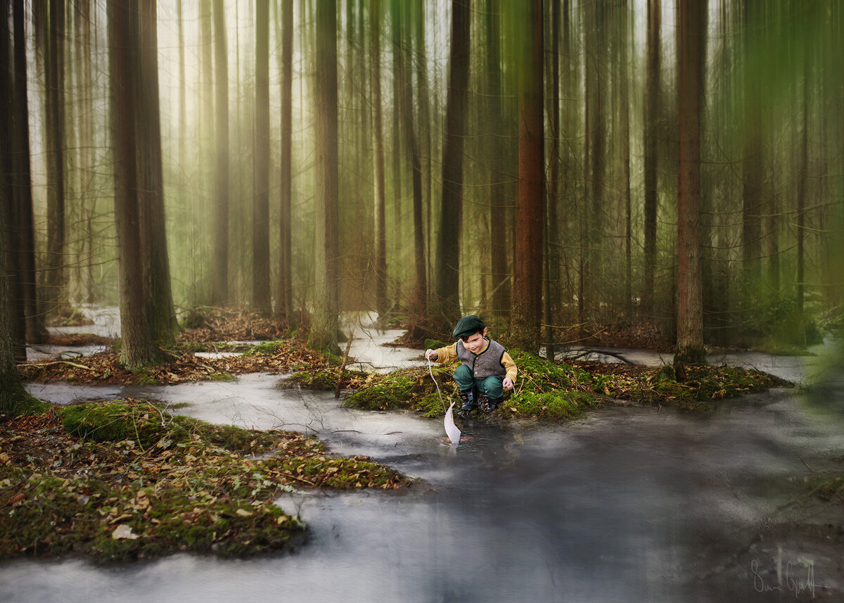 liten pojke i gul tröja, väst, gröna byxor och gubbkep. Sitter och leker med barkbåt i ett landskap  med rinnande vatten och sagolika träd.