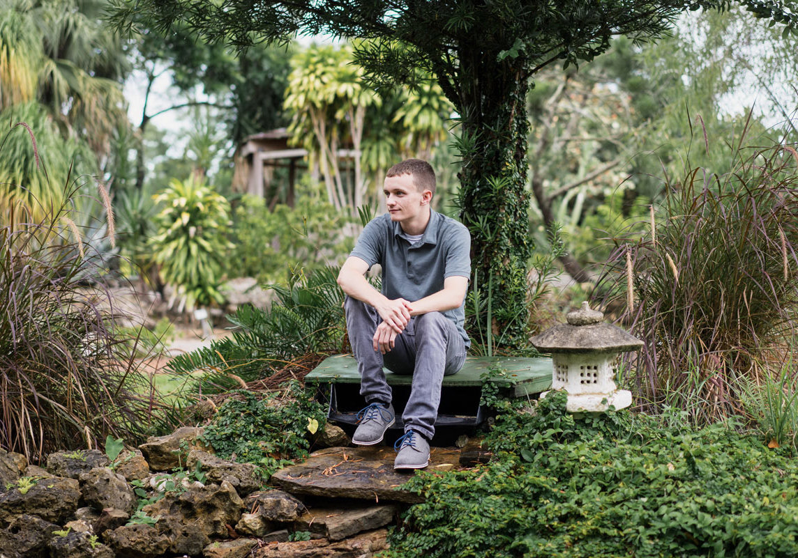 A high school senior boy sitting on a rock looking away