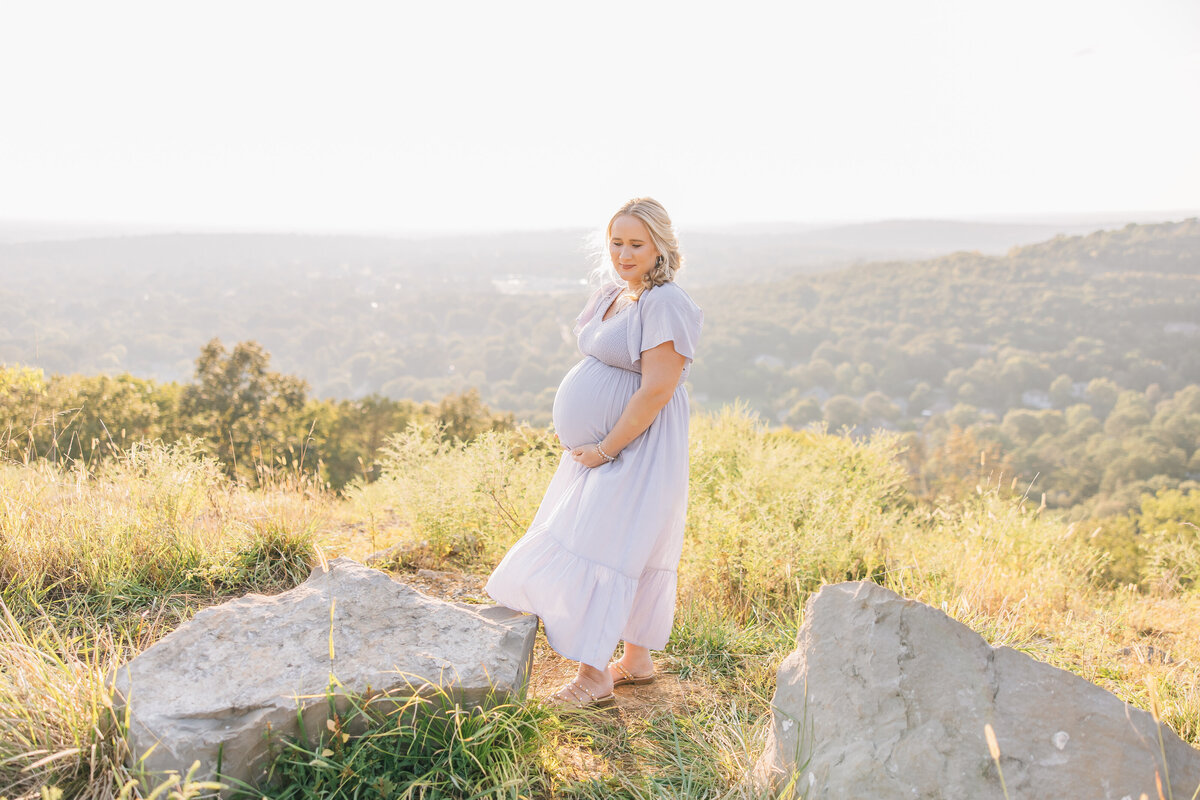 pregnant woman standing next to rocks on a mountain
