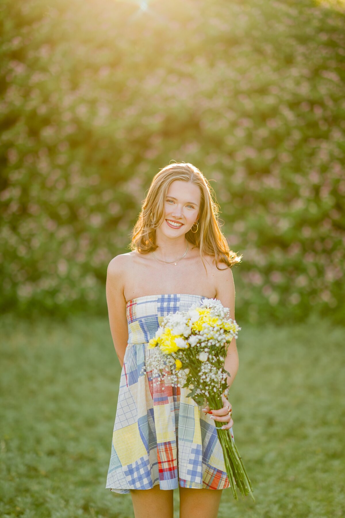 senior girl standing in the grass with the sun surrounding her
