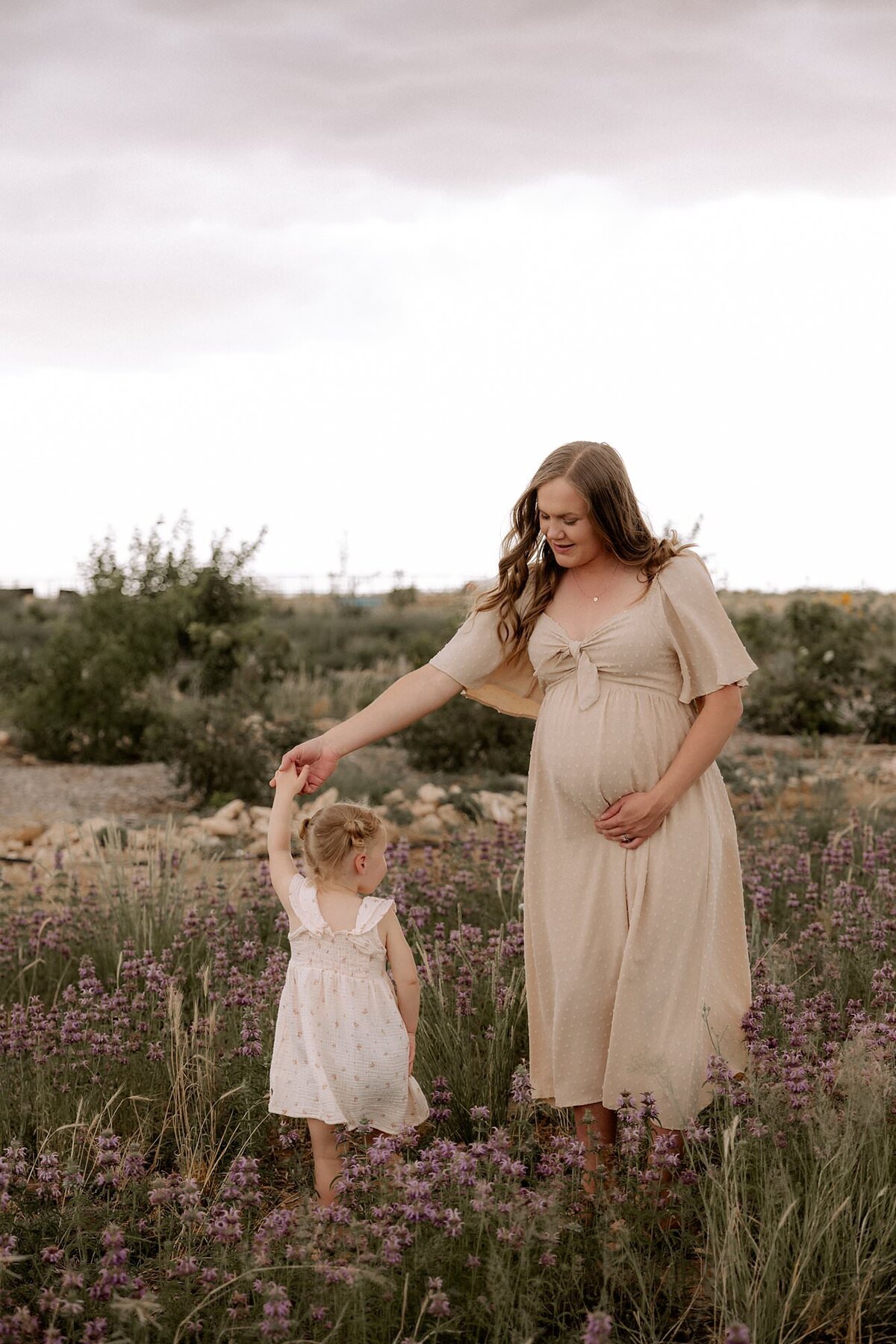 pregnant mom spinning her three year old daughter in a flower field