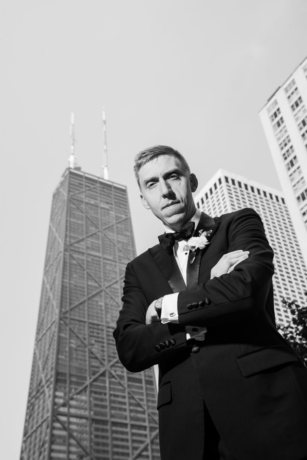 A man in a tuxedo stands in front of a tall building