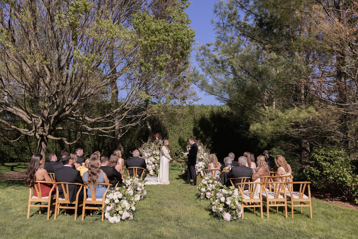 Bride and groom exchange vows in an intimate outdoor wedding ceremony at a private estate in the Hamptons, surrounded by lush spring florals and close family and friends.