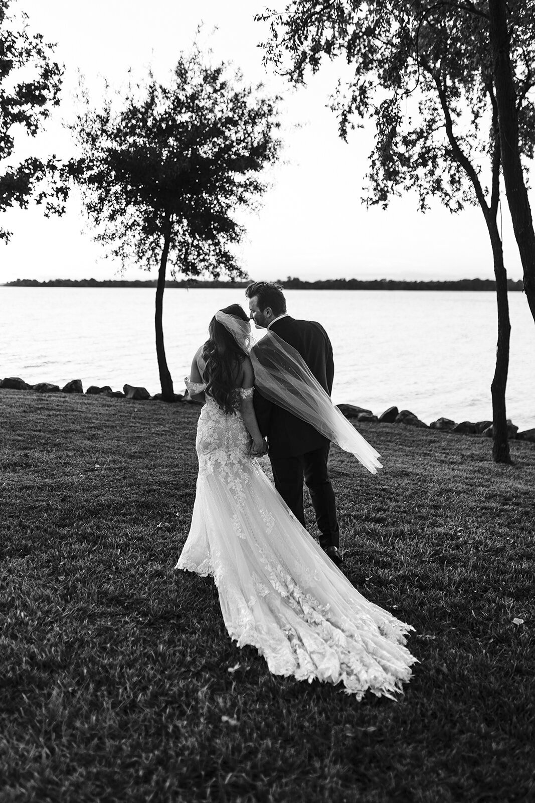 Bride and groom walk hand in hand towards lake