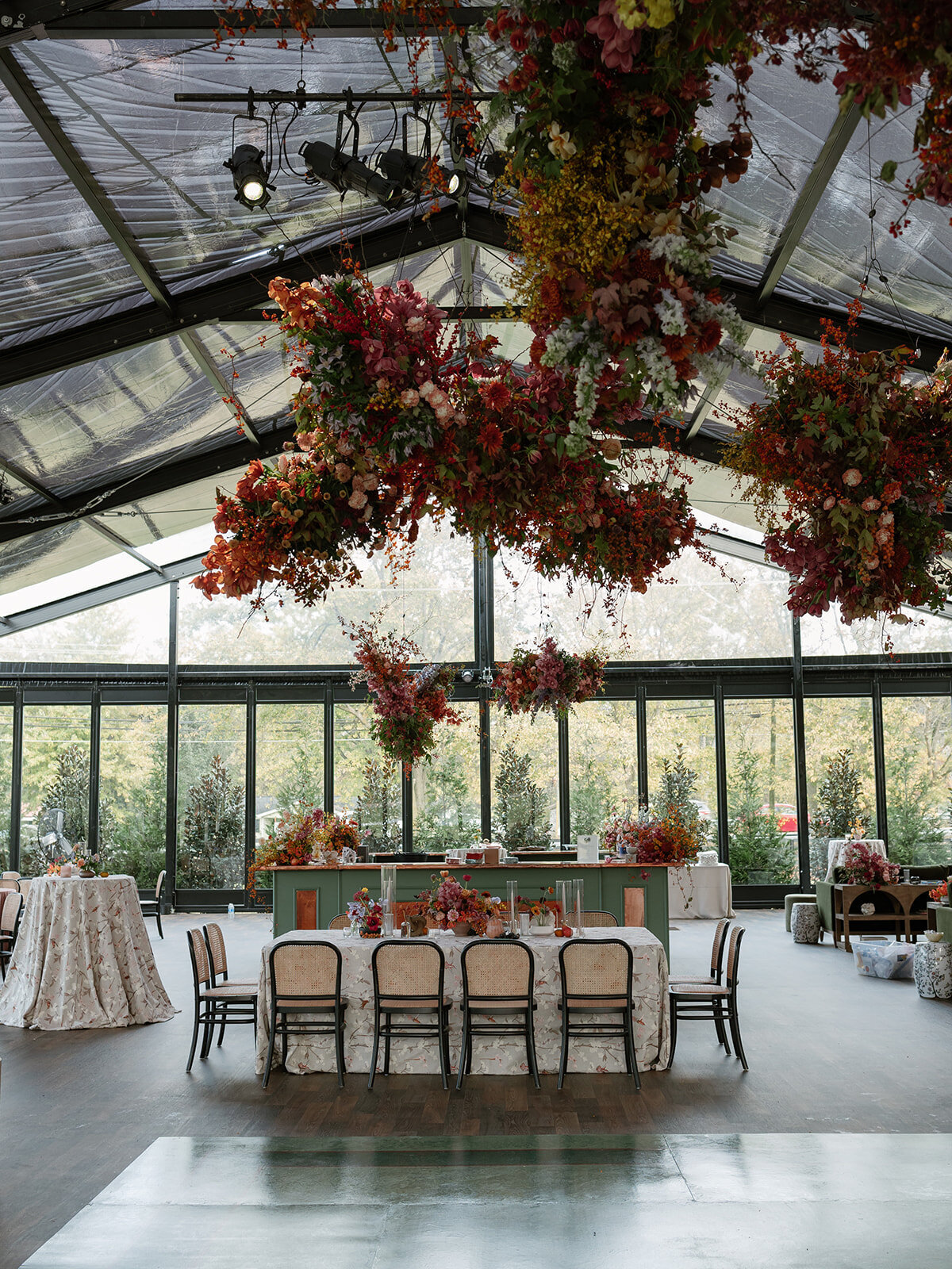 Interacting and sculptural floral clouds hang over the dance floor and bars of this fall wedding reception in Tennessee. Clear top tent build out for fall wedding reception in Tennessee hills.  Product clustered floral clouds in a tasteful fall color palette of copper, ruby, gold, burgundy, rust, and lavender. Orchids, bittersweet berries, butterfly ranunculus, and tulips are highlighted. Unique floral design with flower forward large scale installations. Design by Rosemary & Finch Floral Design in Nashville, TN.