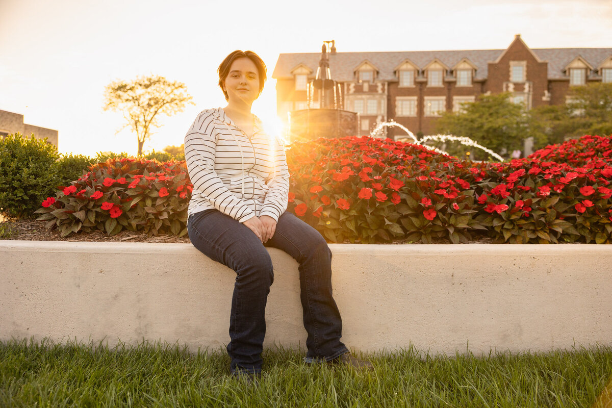A senior girl sitting on a fountain in front of flowers on the KU campus in Lawrence KS
